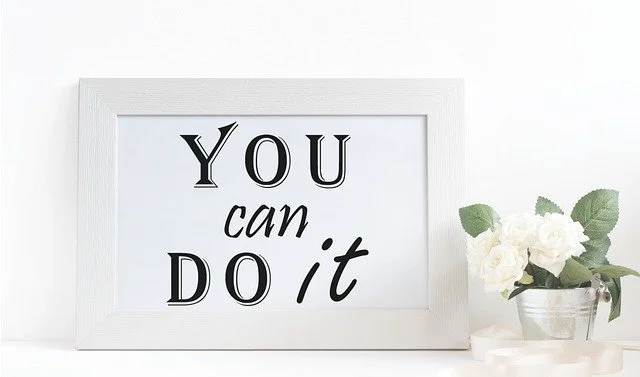 Framed quote saying "You can do it" next to a pot of white flowers with green leaves