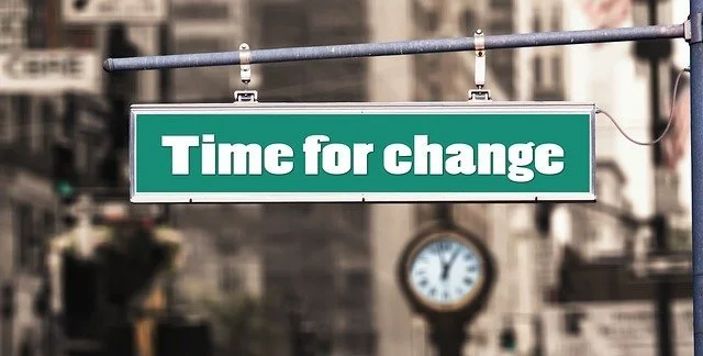 A street sign that reads 'Time for change' with a clock in the blurred city background.