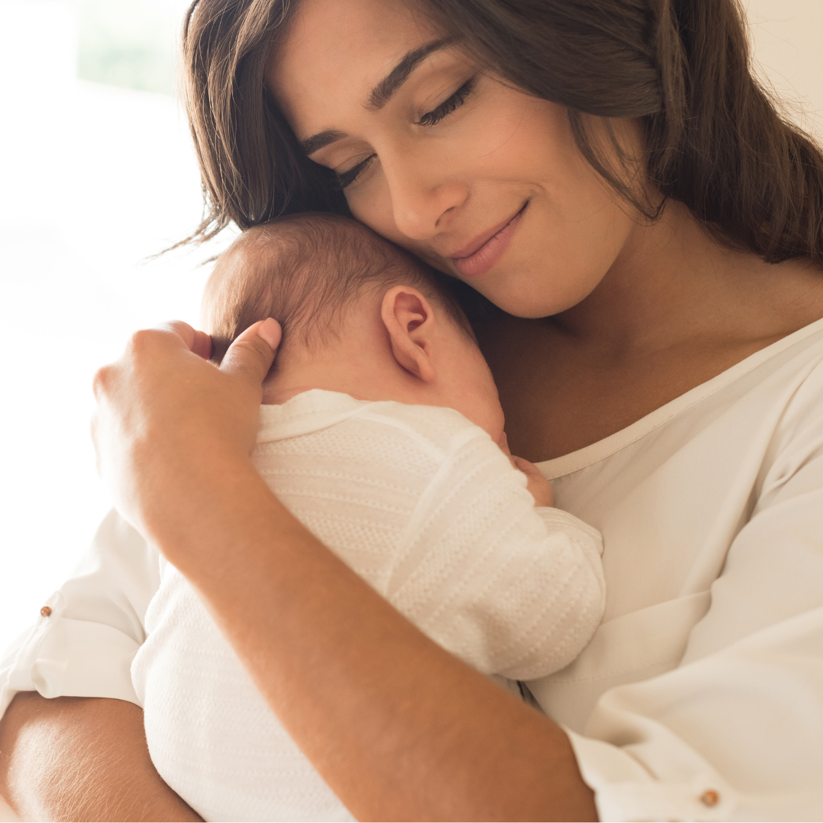 A woman holding a sleeping baby close to her chest with both smiling and eyes closed, showing tender affection.