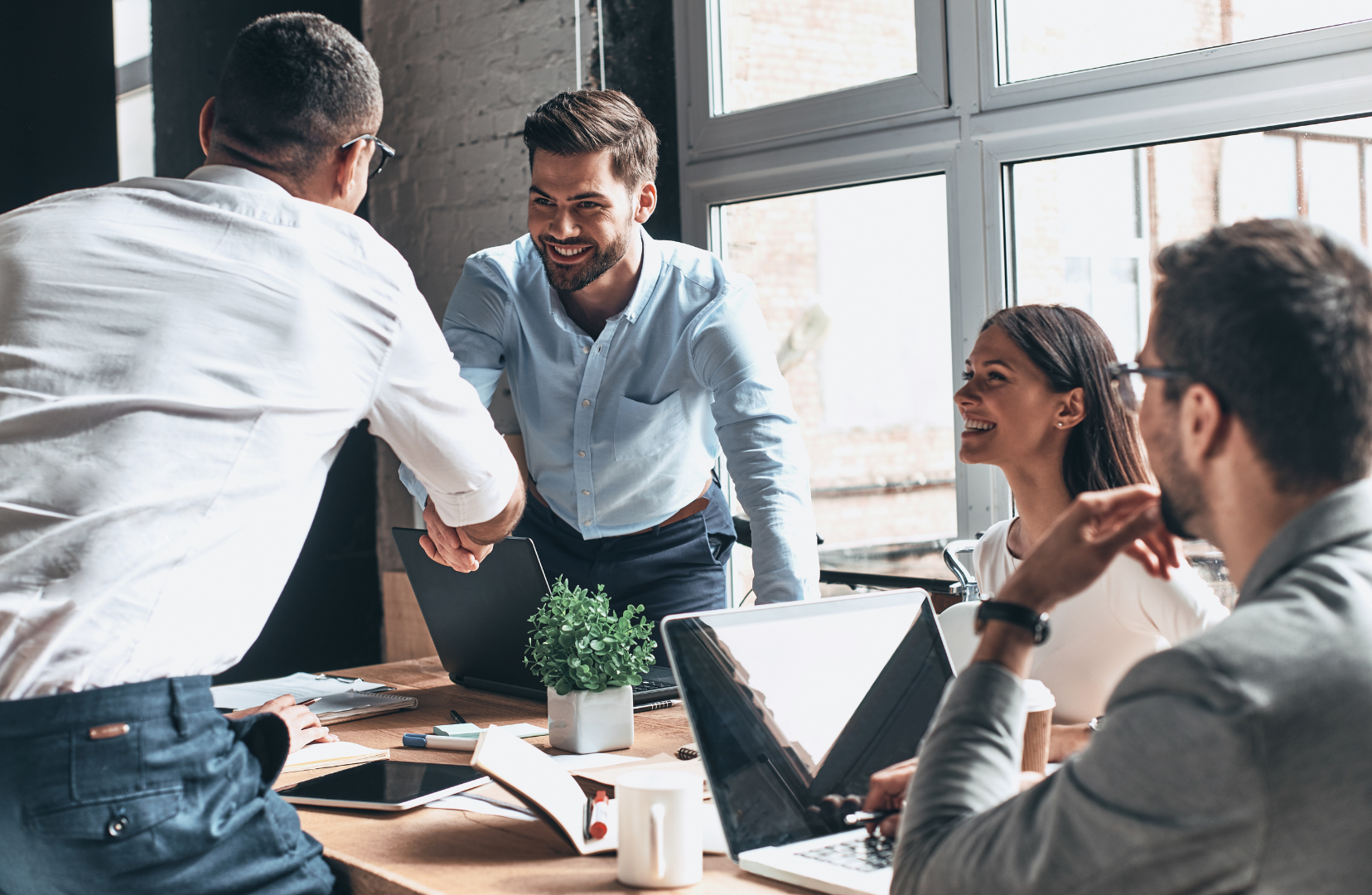 Group of five diverse colleagues in a business meeting in a modern office, , shaking hands and smiling.