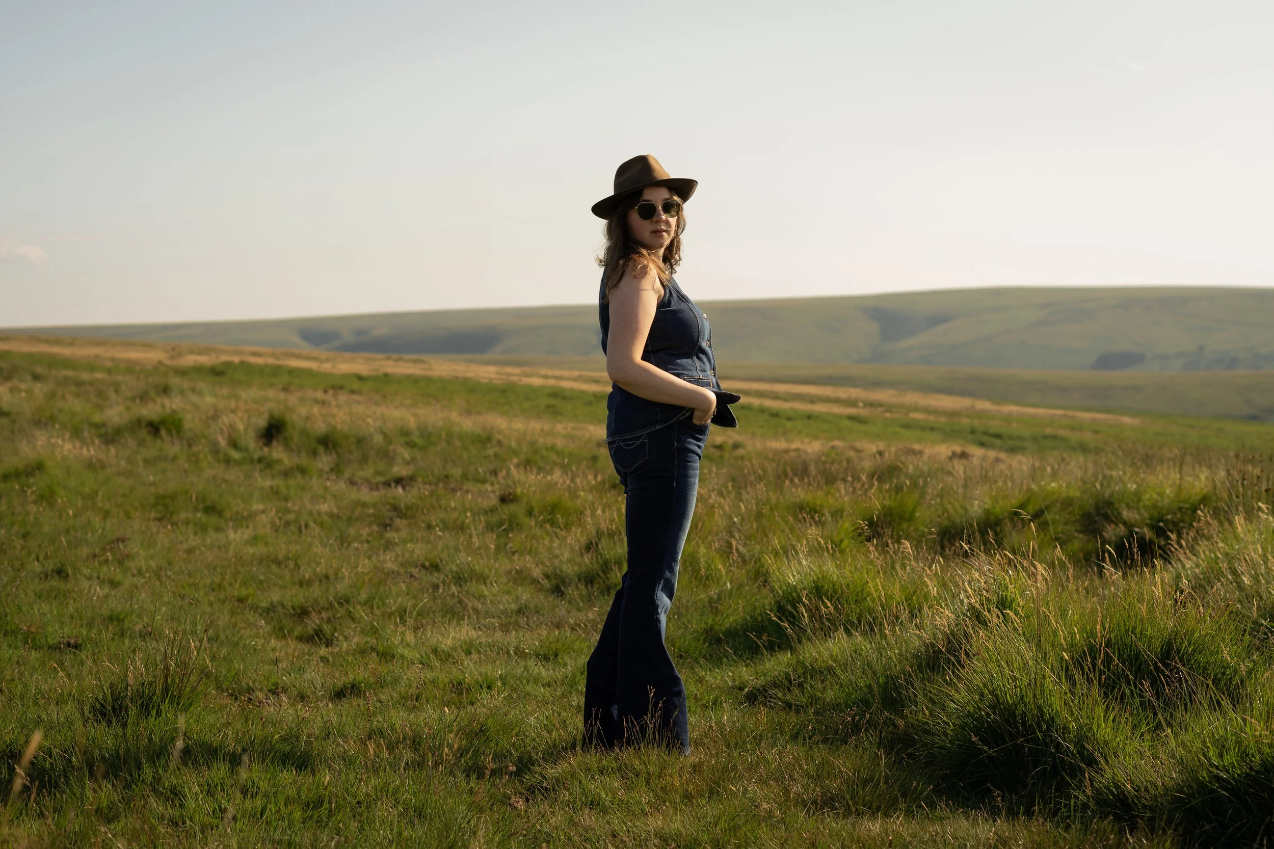 woman turning back in wide open green space with sunglasses and a hat on