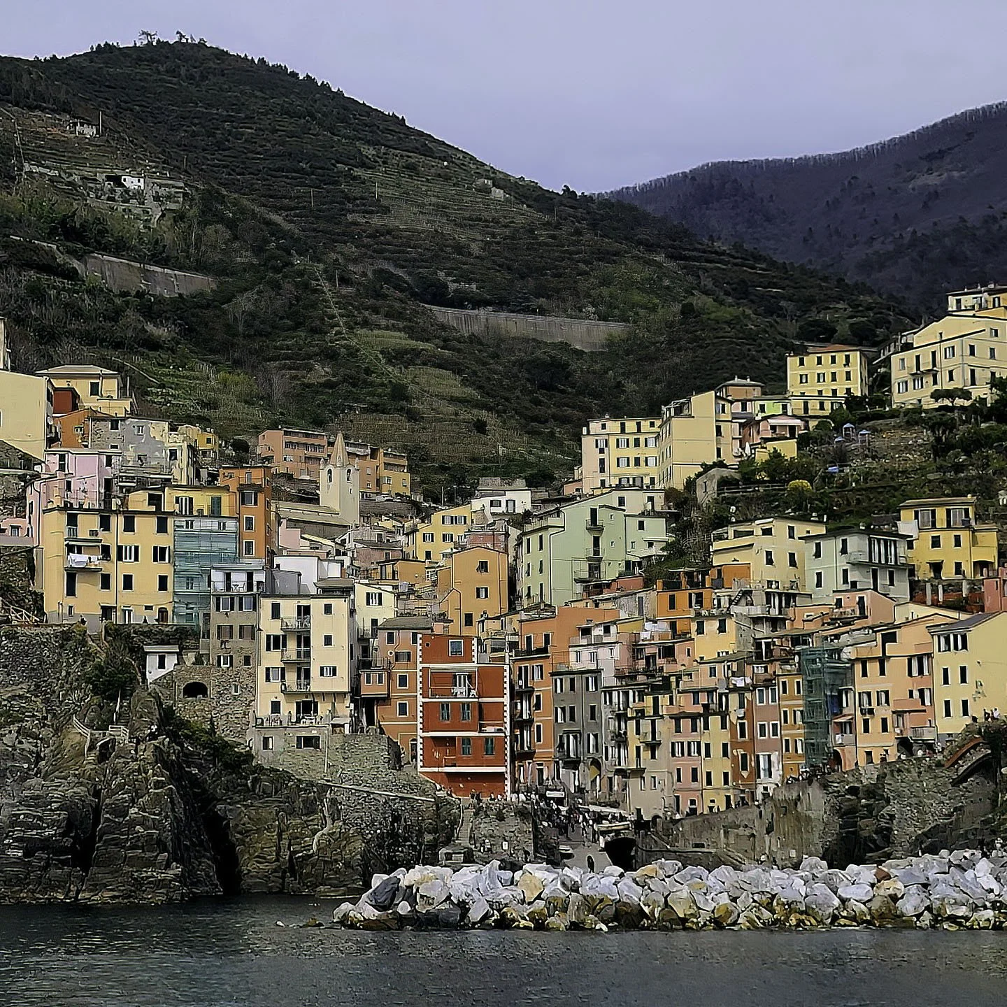 Colorful houses built into hillsides along the coast, with a rocky shoreline and water in the foreground.