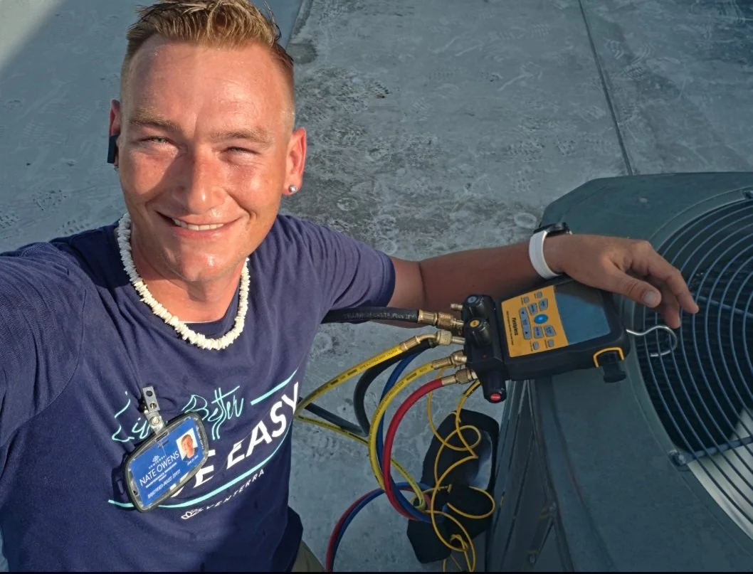 A smiling technician working on an air conditioning unit with gauges and hoses attached, outdoors on a rooftop.