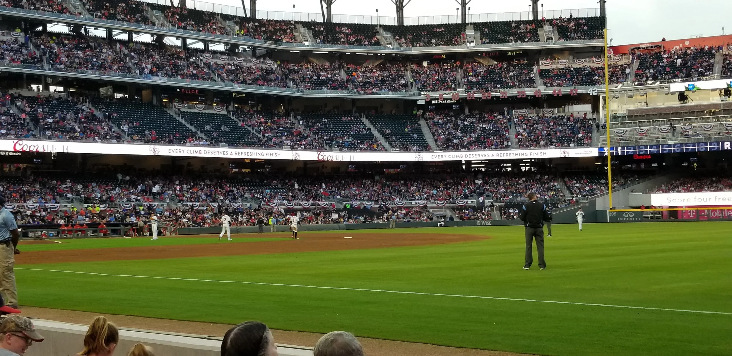 Baseball game in a stadium filled with spectators, players on the field, and advertising banners around the outfield.