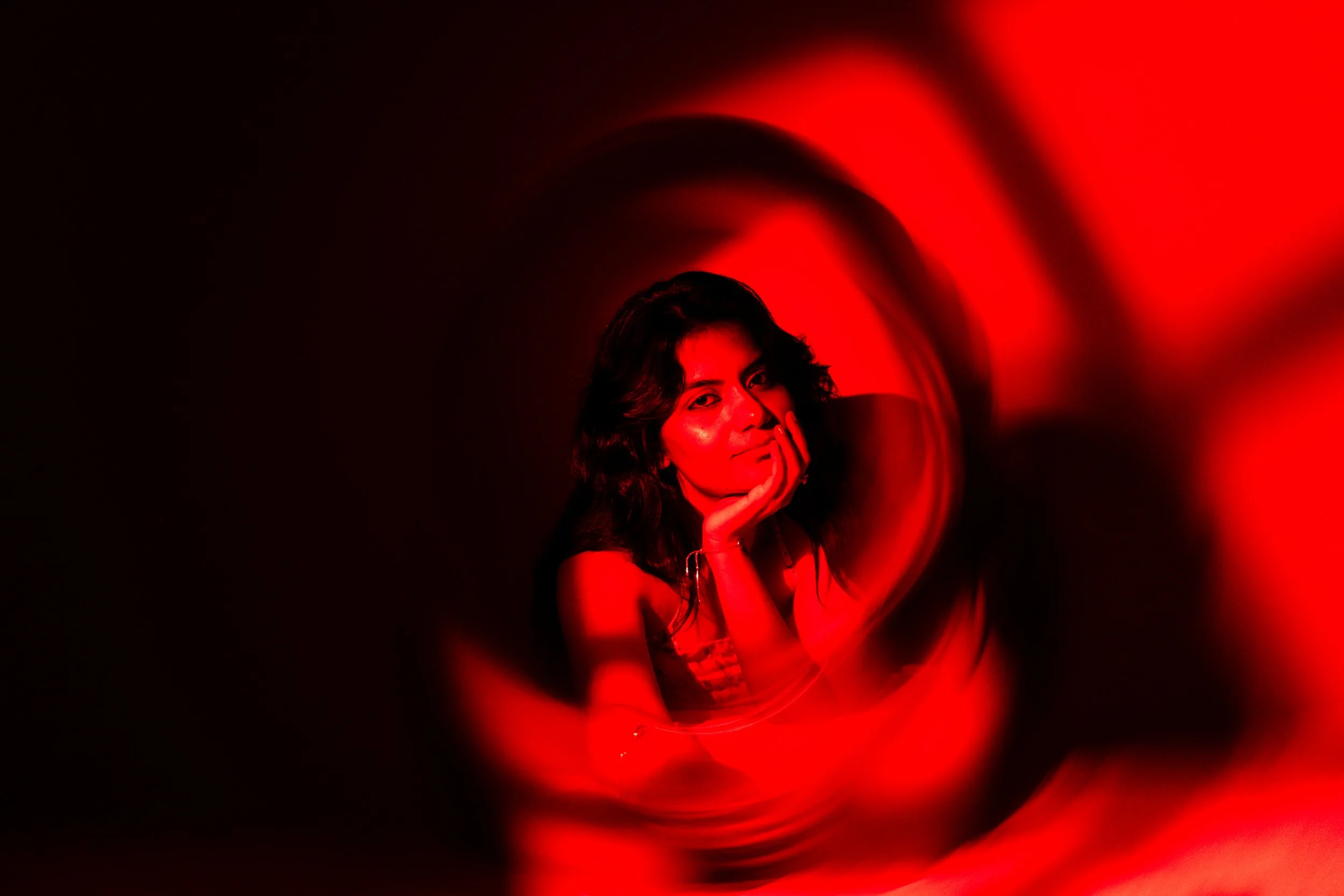 A woman with dark hair leaning her chin on her hand, surrounded by a red light swirling around her.