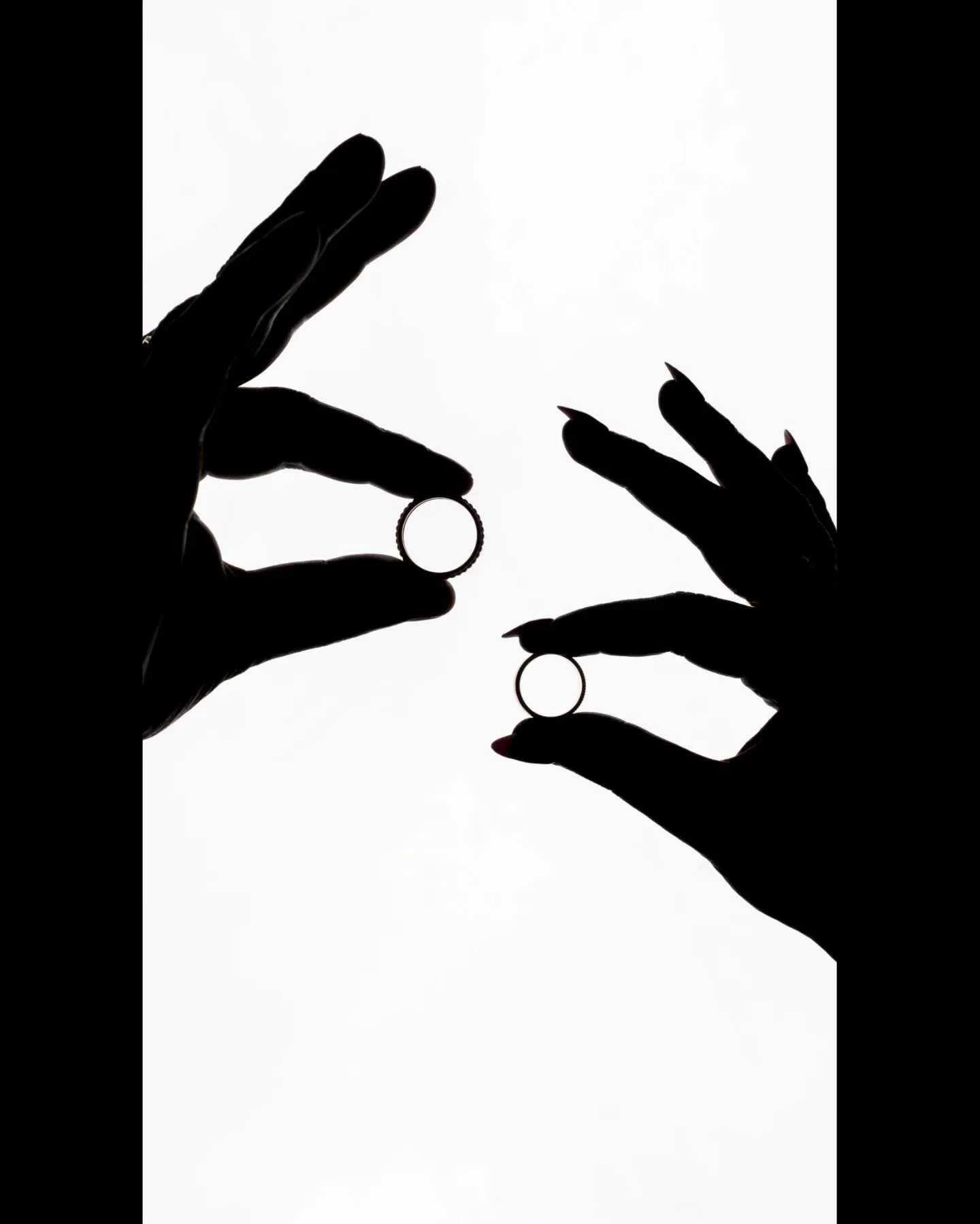 Silhouette of two hands holding wedding rings against a white background.