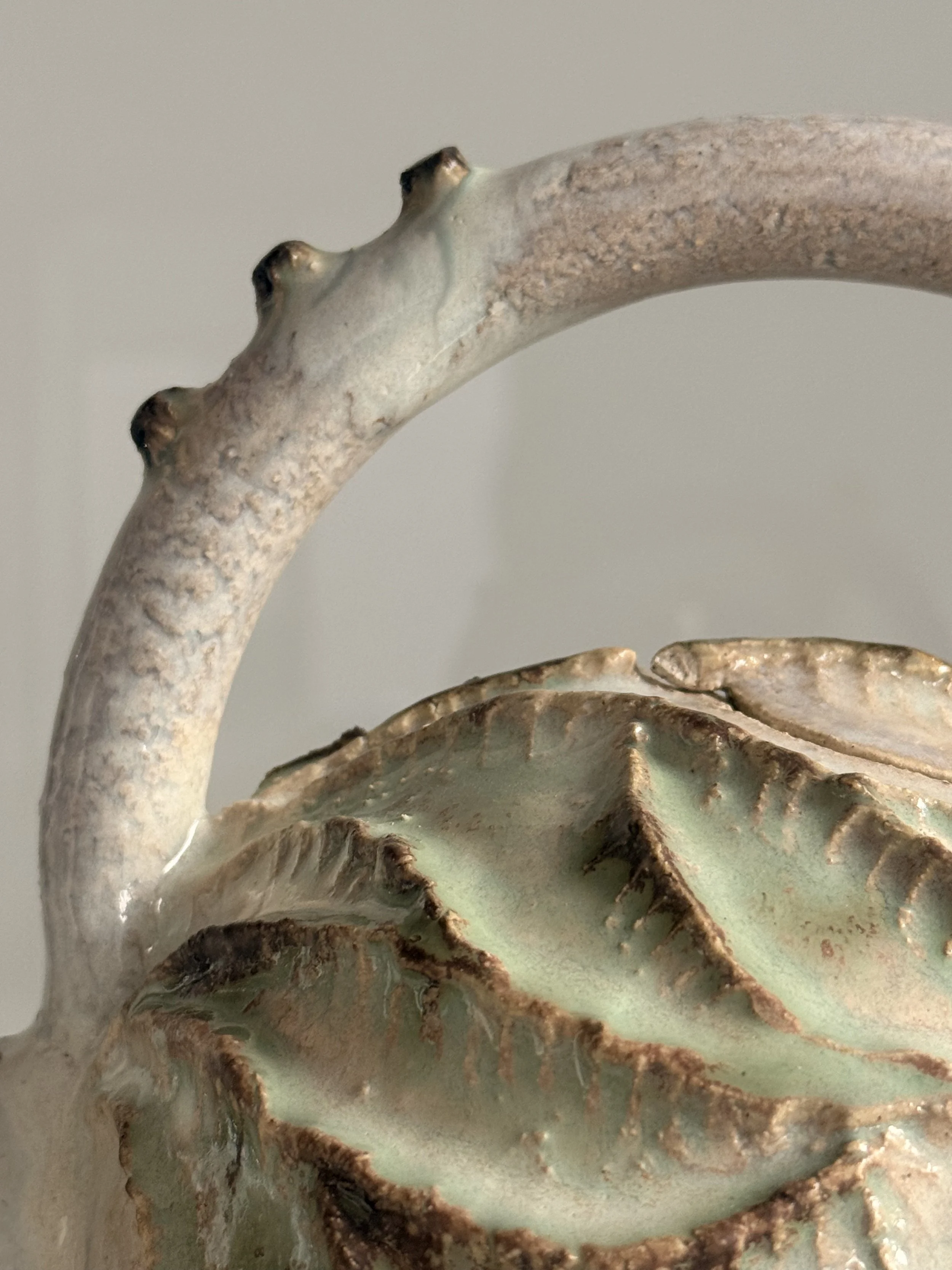 Close-up of a decorative ceramic or metal vase with a textured, ruffled rim and a curved handle.