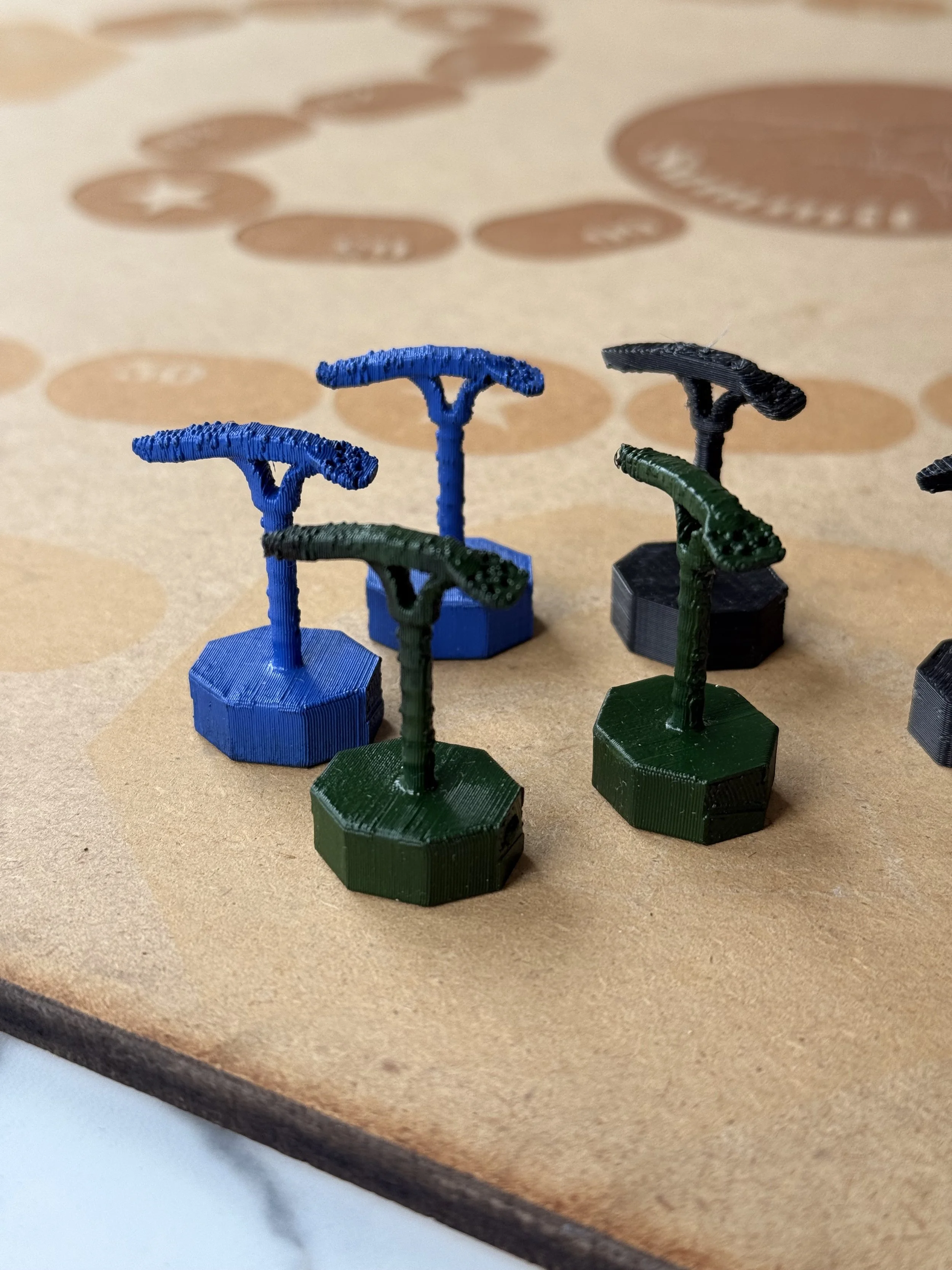 Close-up of green and blue 3D-printed chess pawns on a wooden surface, with shadowed circular patterns in the background.