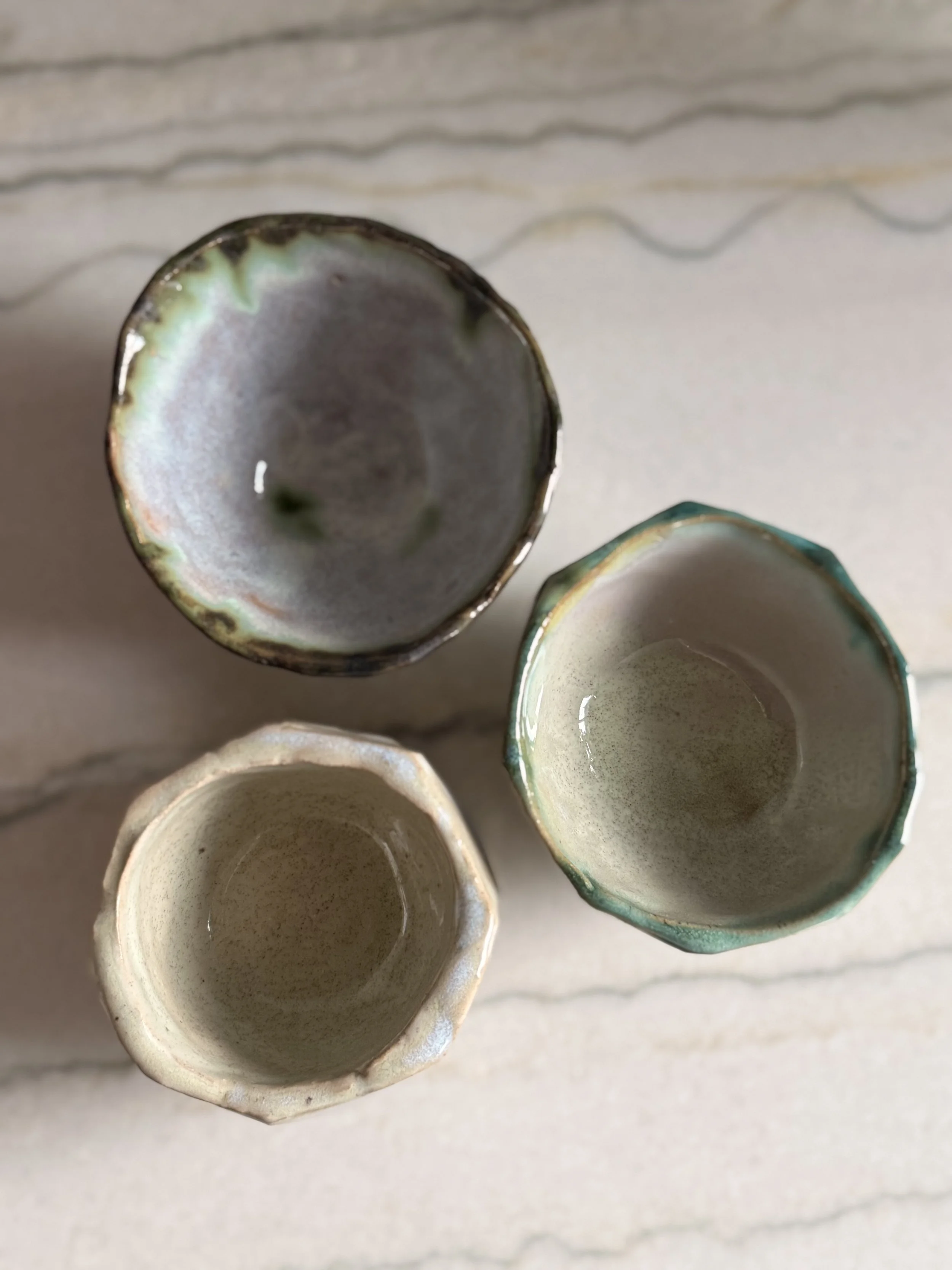 Top view of four small, empty ceramic cups with varying pastel-colored rims, arranged on a white surface.
