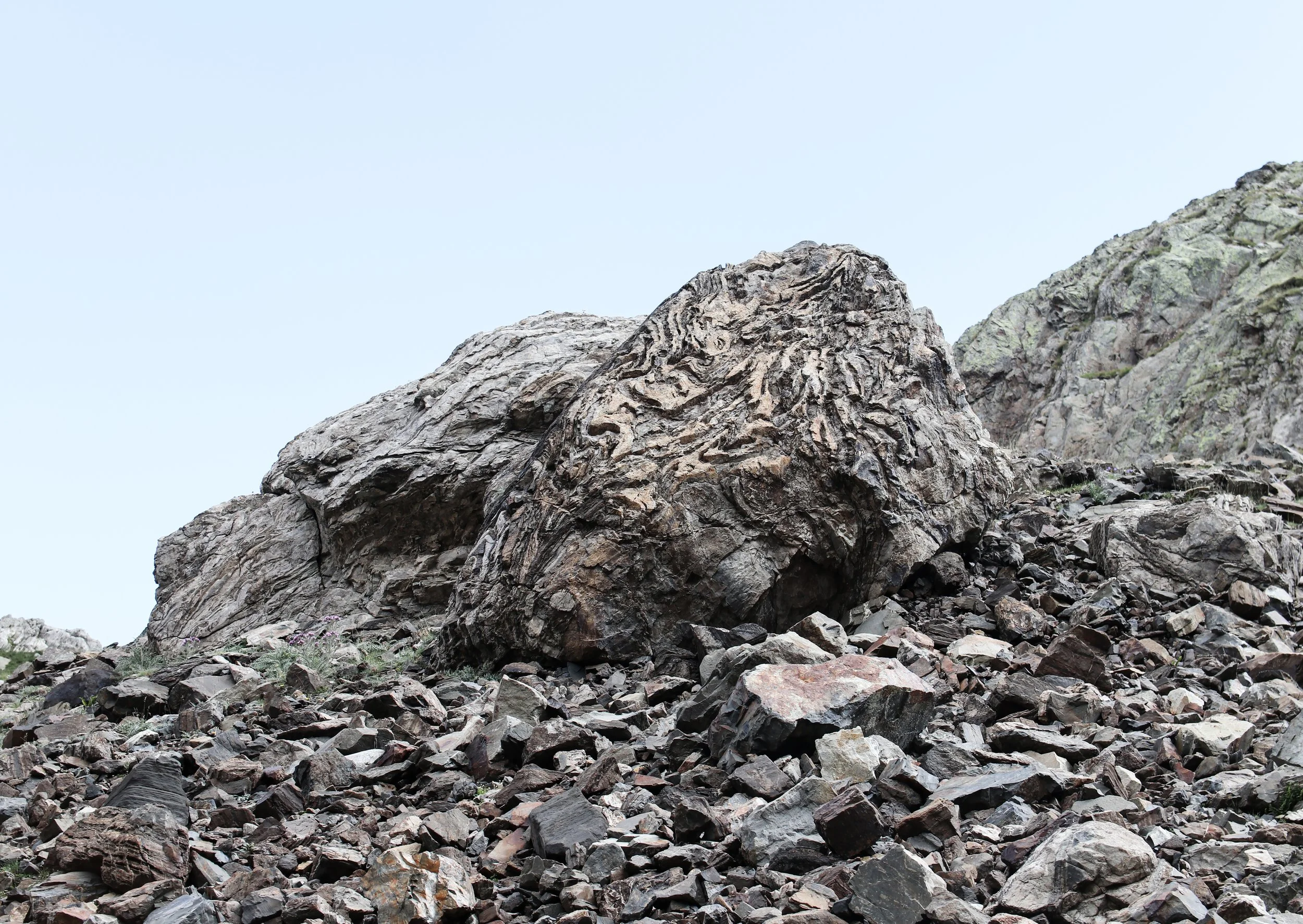 Close-up of rugged, textured rocks and boulders at the base of a mountain with a clear blue sky in the background.