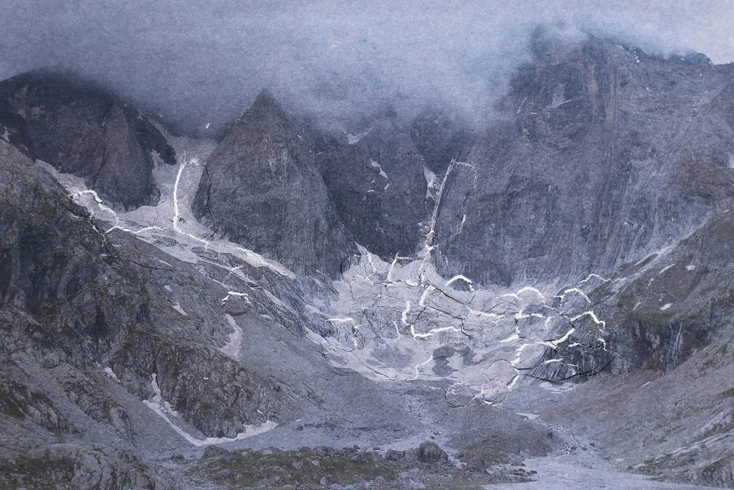 A mountain landscape with rugged peaks partly covered in fog, with snow and rock formations in the valley.
