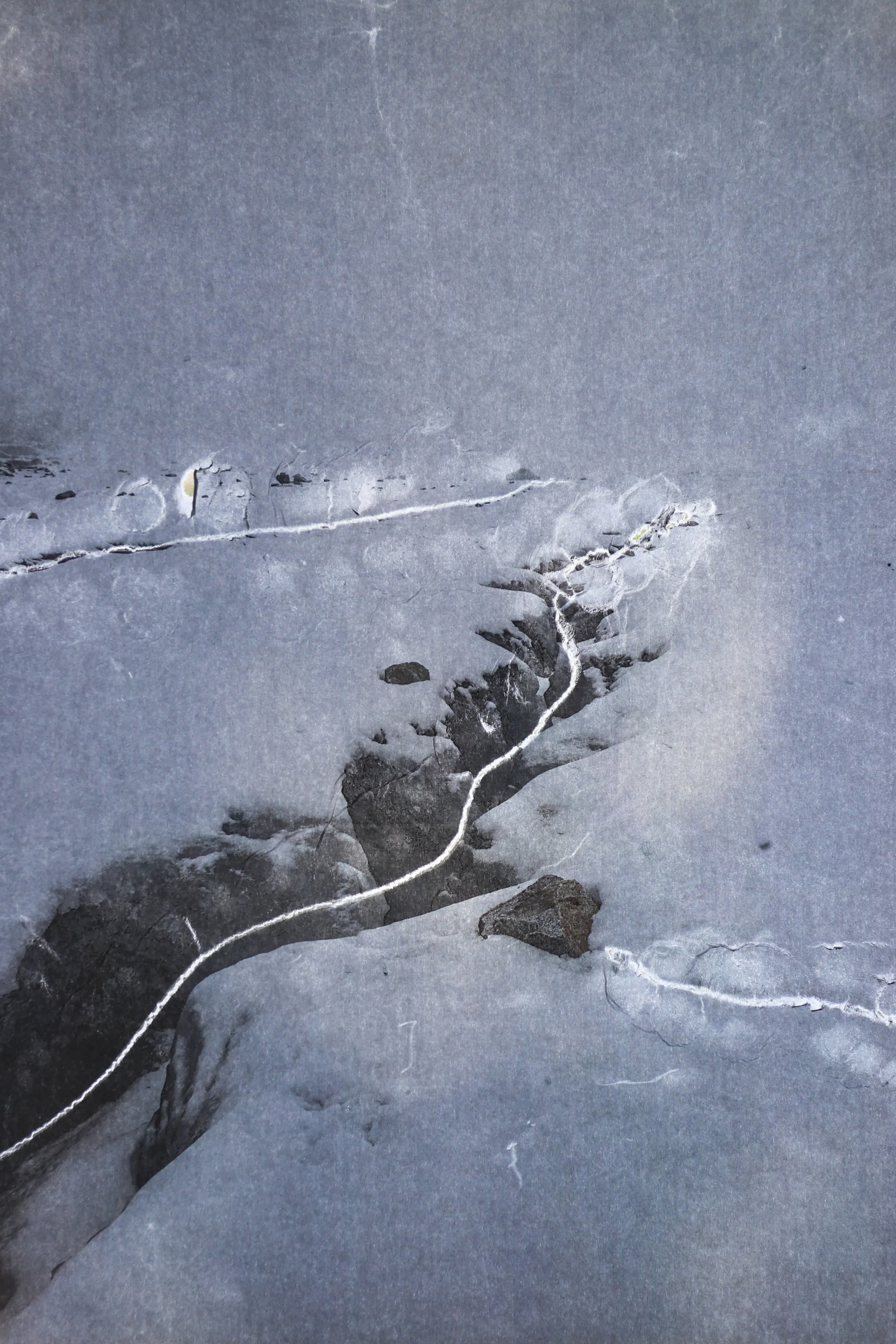 Snow-covered ground with a crack running through and rocks scattered around.