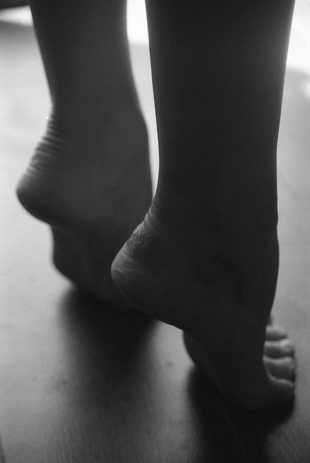Close-up of bare feet and ankles on a wooden floor, black and white photo.