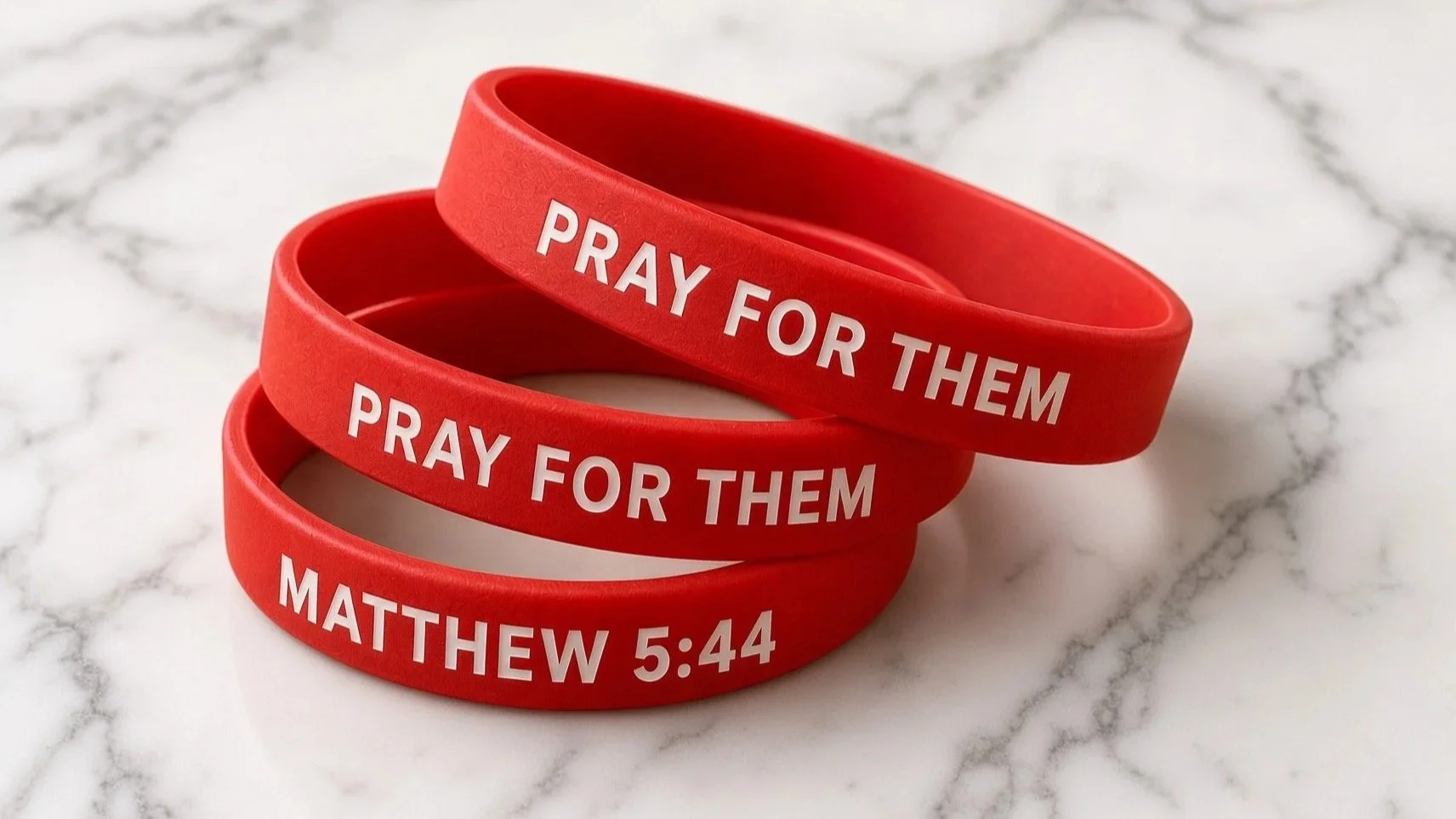 Signature red waterproof MATTHEW 5:44 CHALLENGE bracelets reading "PRAY FOR THEM" with the additional text "MATTHEW 5:44," placed on a white marble surface.