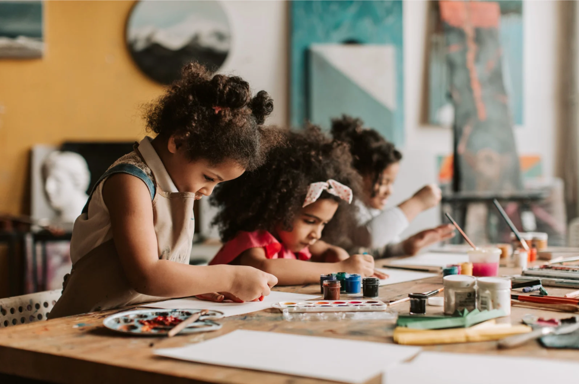 Children engaged in painting and art activities at a table in an art studio.
