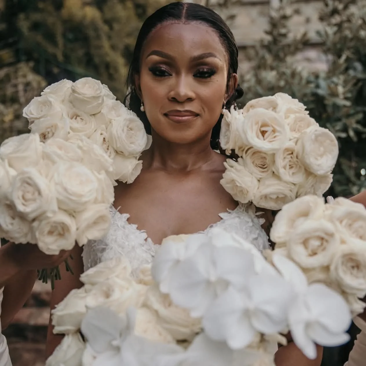 A woman dressed in a white gown holding large bouquets of white roses.