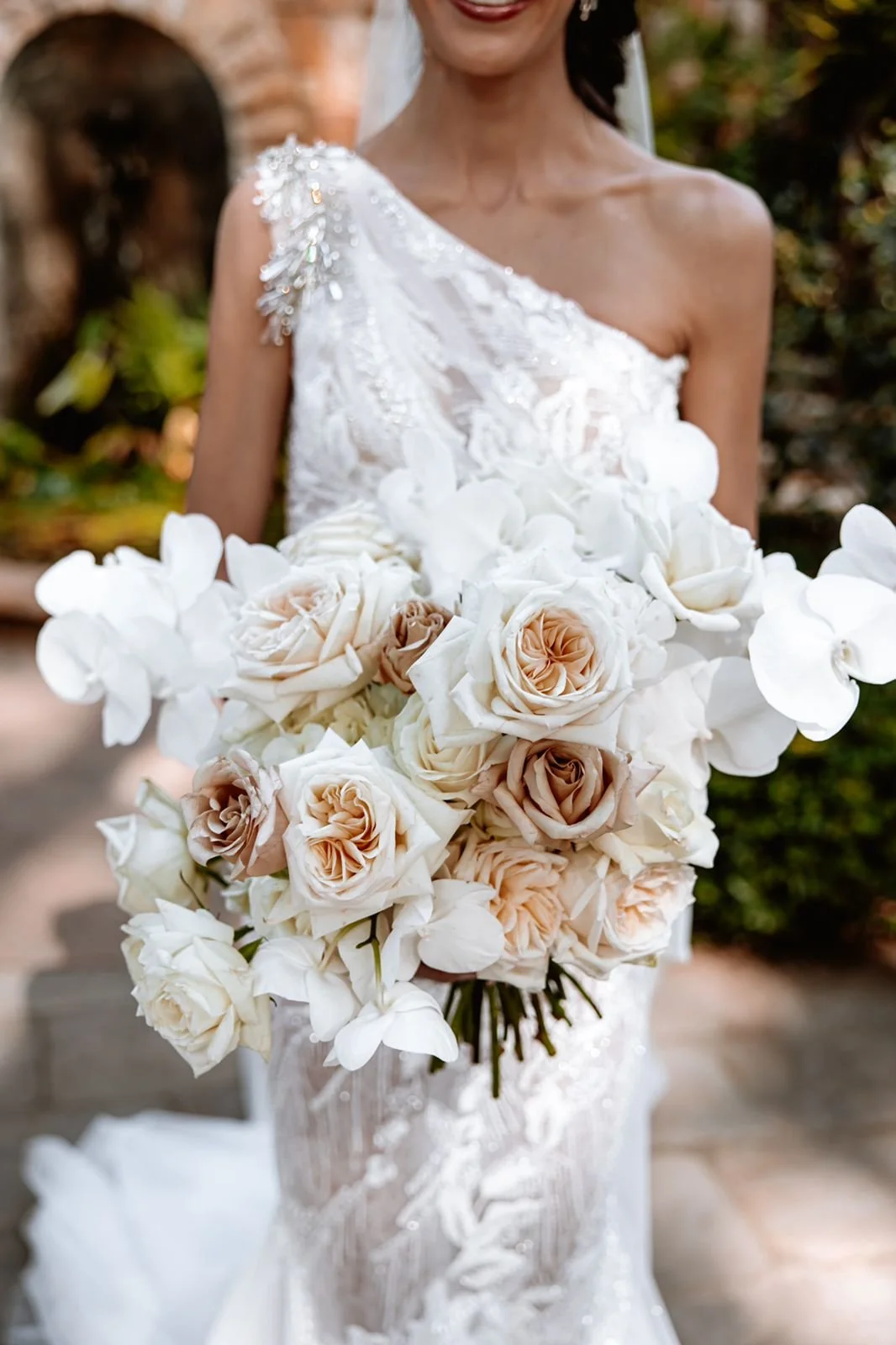 Bride in a white wedding dress holding a large bouquet of white, nude and blush roses and orchids.