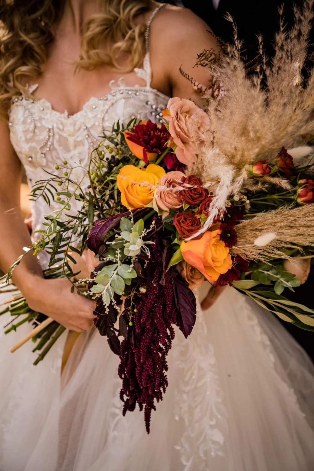 A bride in a white dress holding a colorful bouquet of flowers with pampas grass and greenery.