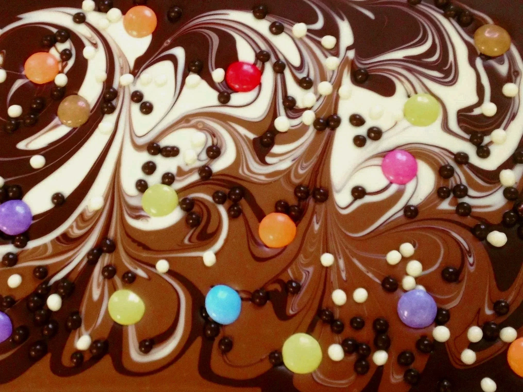 Schokoladentafel mit bunten Streuseln und Dekoration aus weißer, dunkler und Milchschokolade in einem Wirbelmuster.