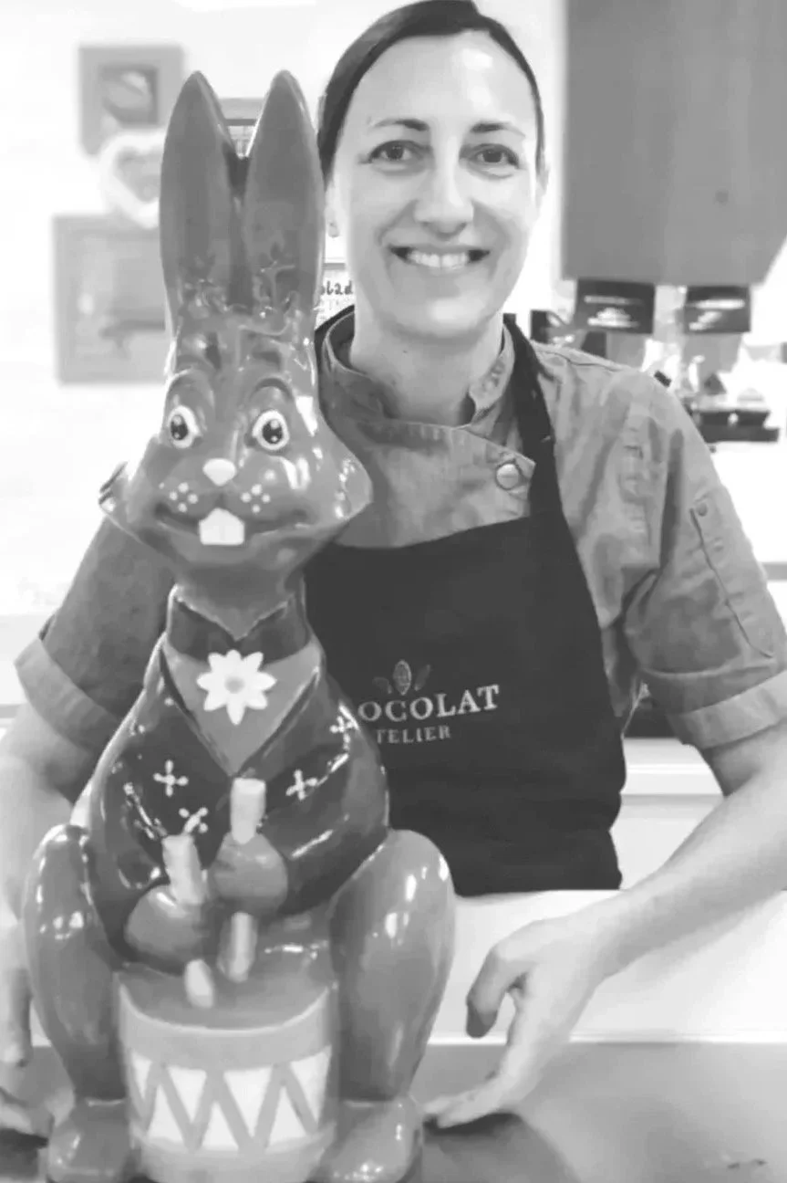 Eine Frau mit Schürze posiert neben einer großen Osterhasenfigur aus Schokolade.