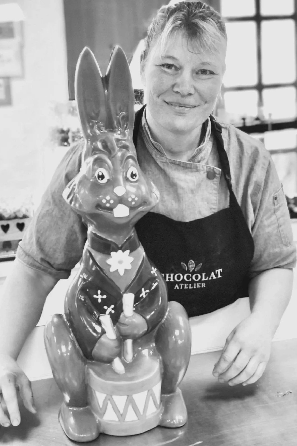 Eine Frau mit Schürze posiert neben einer grossen Osterhasenfigur aus Schokolade.