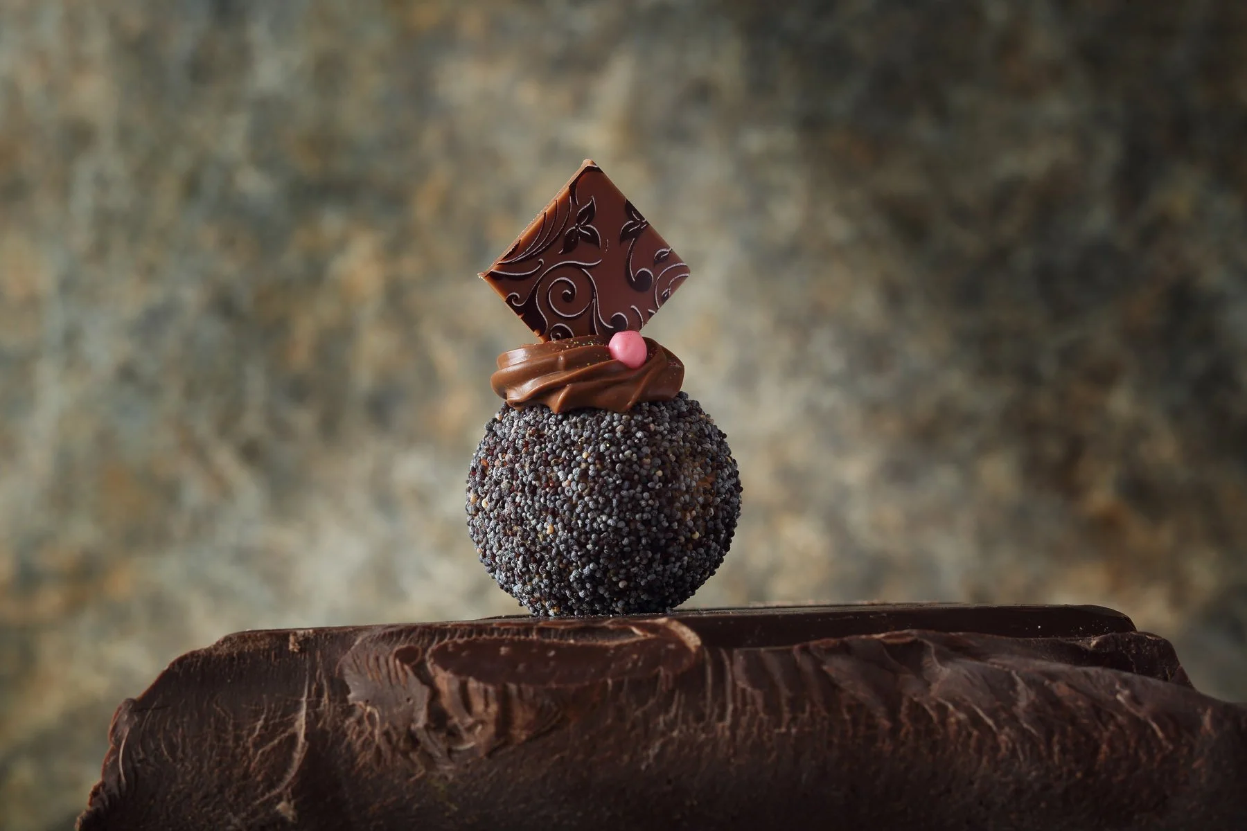 Eine kunstvoll verzierte Praline auf einem Schokoladenblock.