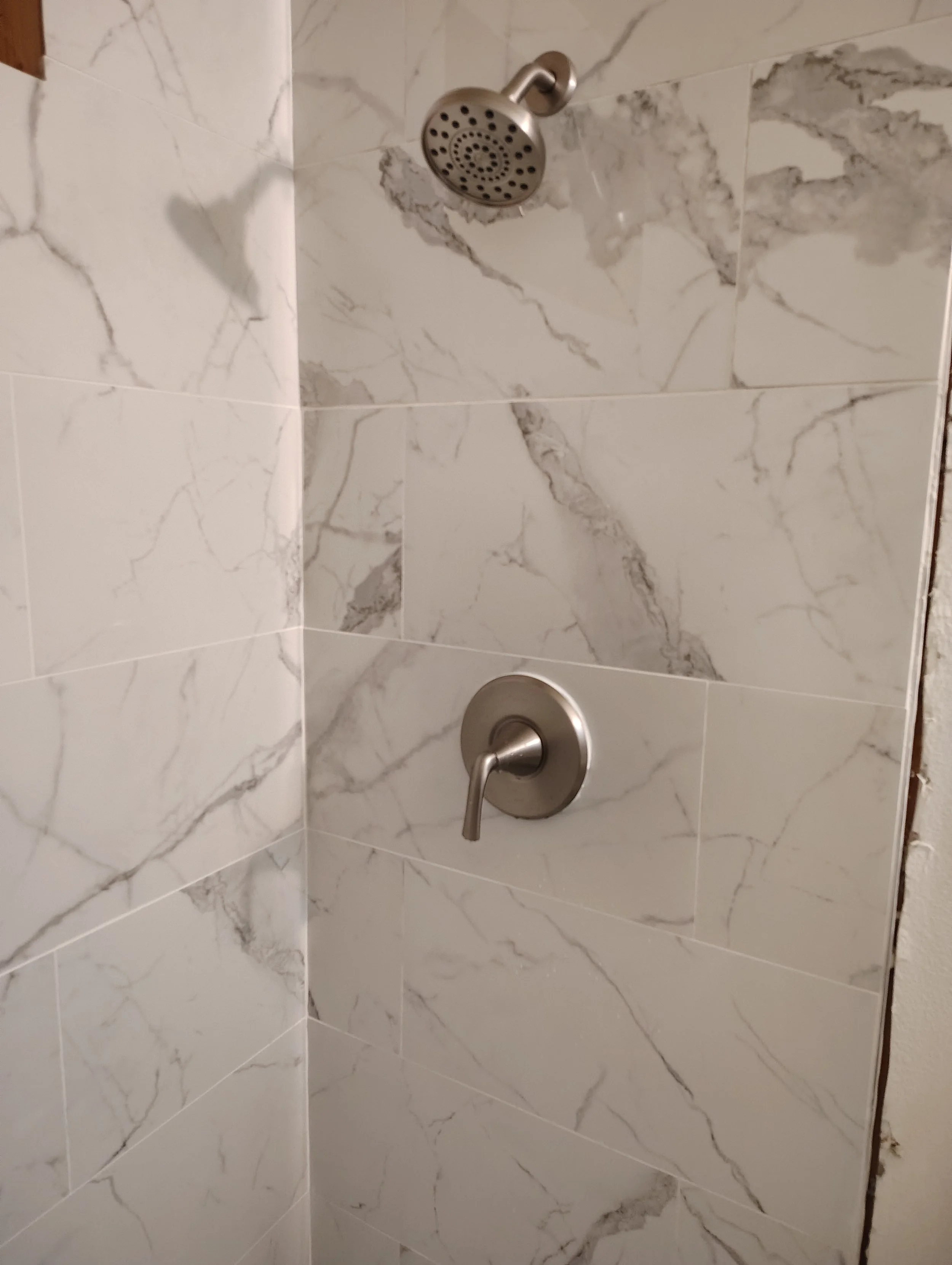 Shower with marble-style tiles, a round showerhead, and a control handle.