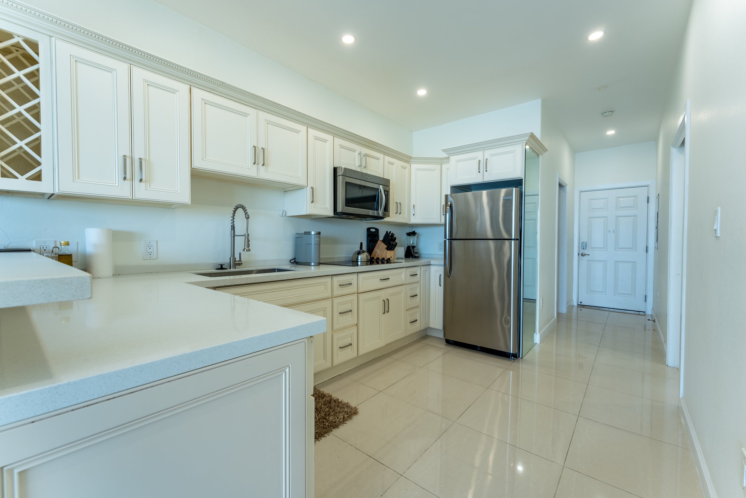 Kitchen with white cabinets, stainless steel refrigerator, oven, microwave, black countertop appliances, and beige tiled floor.