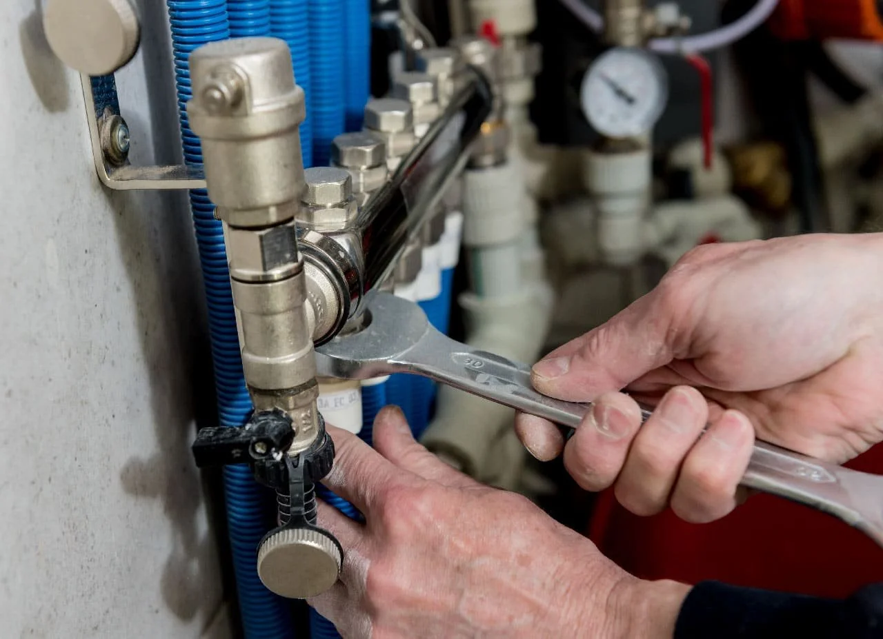 Mani che usano una chiave inglese per lavorare su tubi e raccordi meccanici in un ambiente industriale o di manutenzione.