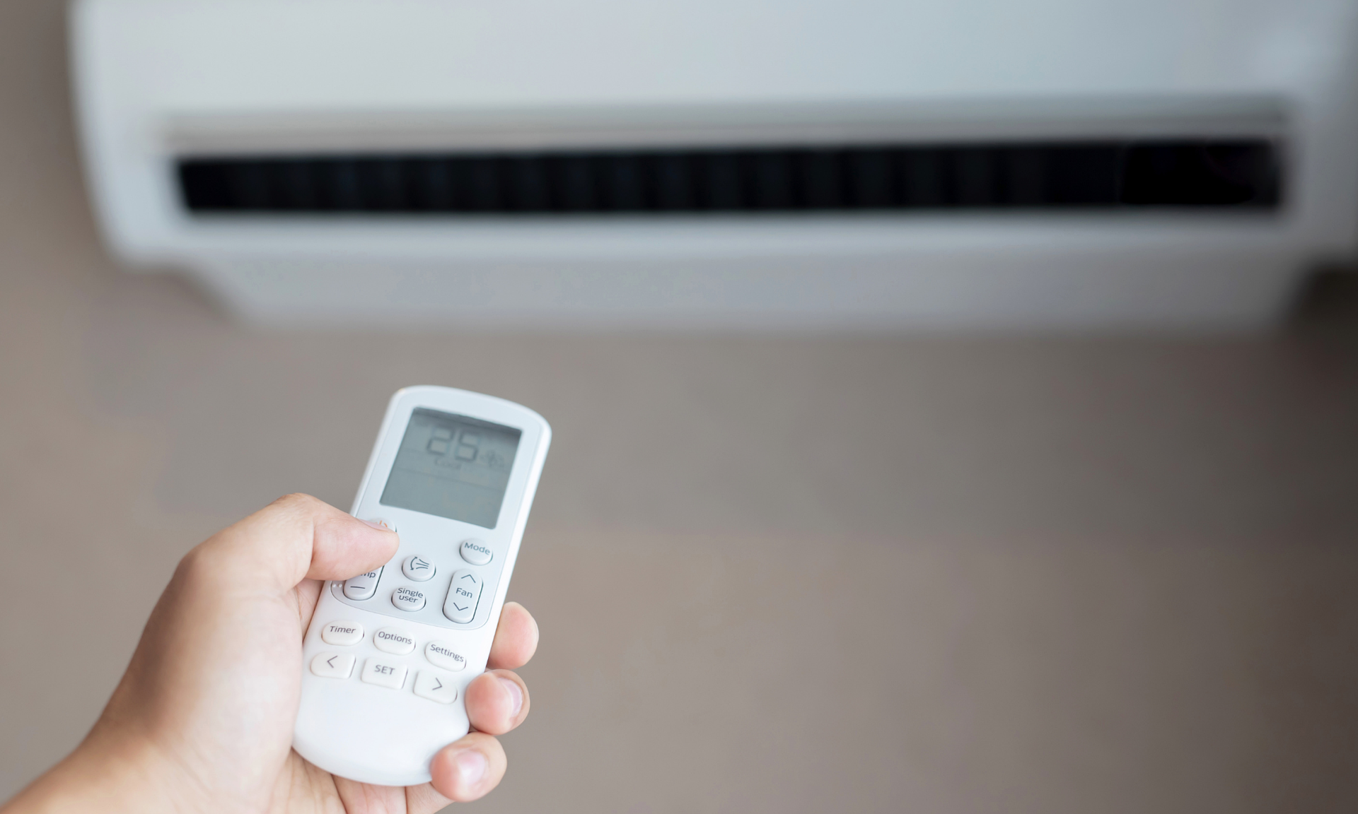 Una mano tiene un telecomando bianco e una temperatura di 25°C, puntando verso un'unità di condizionamento dell'aria a soffitto.