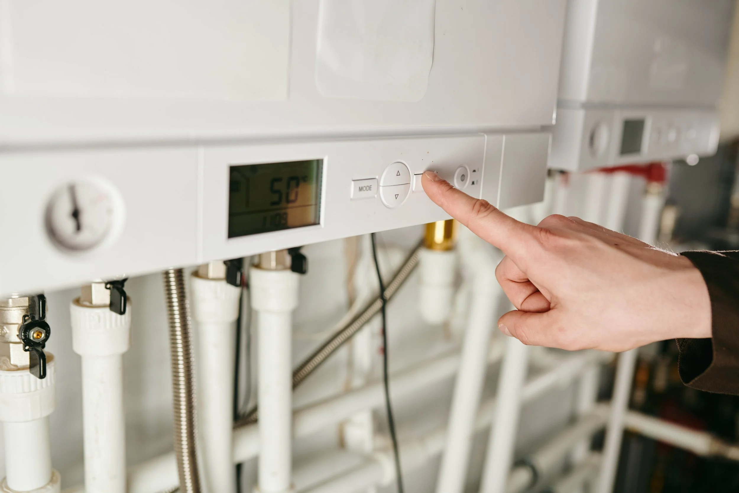 Una mano di una persona sta premendo un pulsante su un dispositivo di controllo di un impianto di riscaldamento o di acqua calda, con un display digitale che mostra 50°.