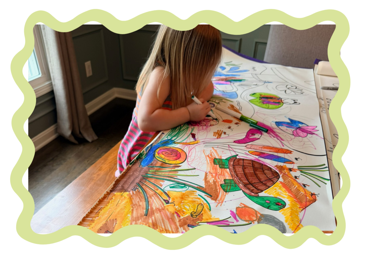 A young girl with blonde hair drawing and coloring on a large sheet of paper on a table. The sheet features colorful drawings of animals and objects, including a turtle, a dragonfly, and a snail, with various vibrant colors.