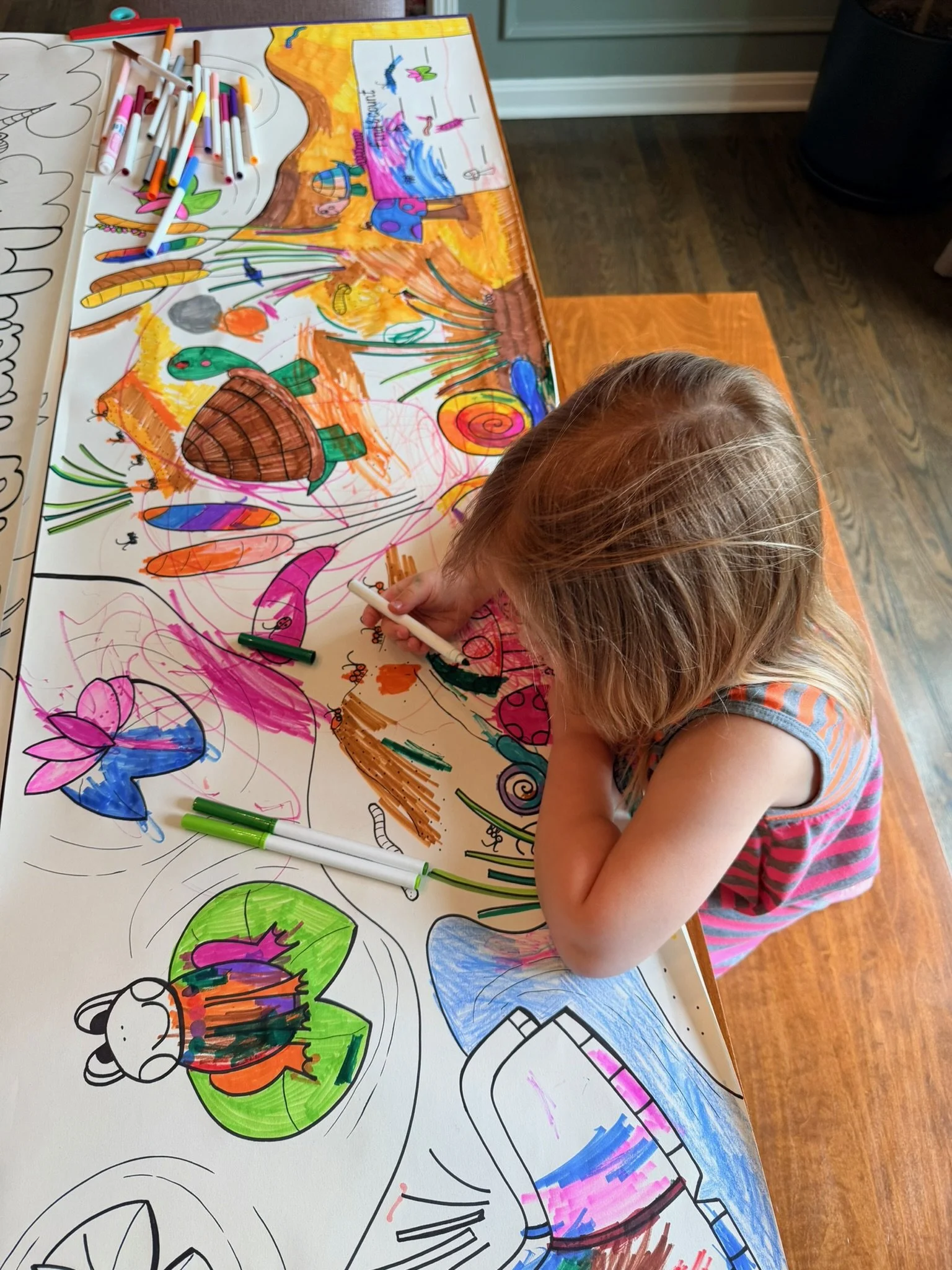 Child coloring and drawing on a large sheet of paper with markers, creating colorful illustrations of animals and nature scenes.