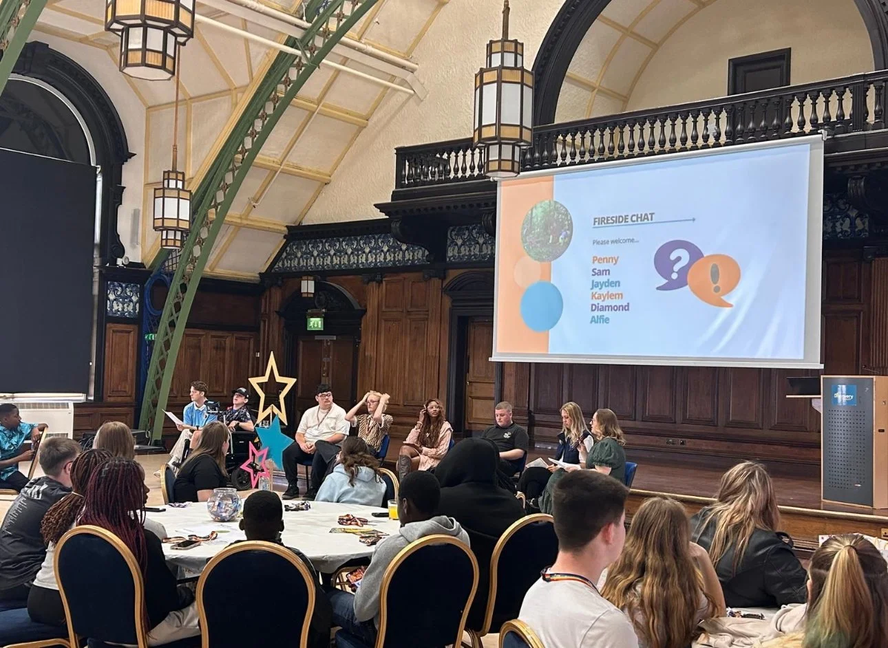 Rylie Sweeney hosts a fireside chat with a group of young people, discussing their experiences and perspectives in front of an audience.