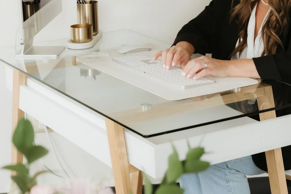 Person working on a computer at a glass-top desk in an office setting.