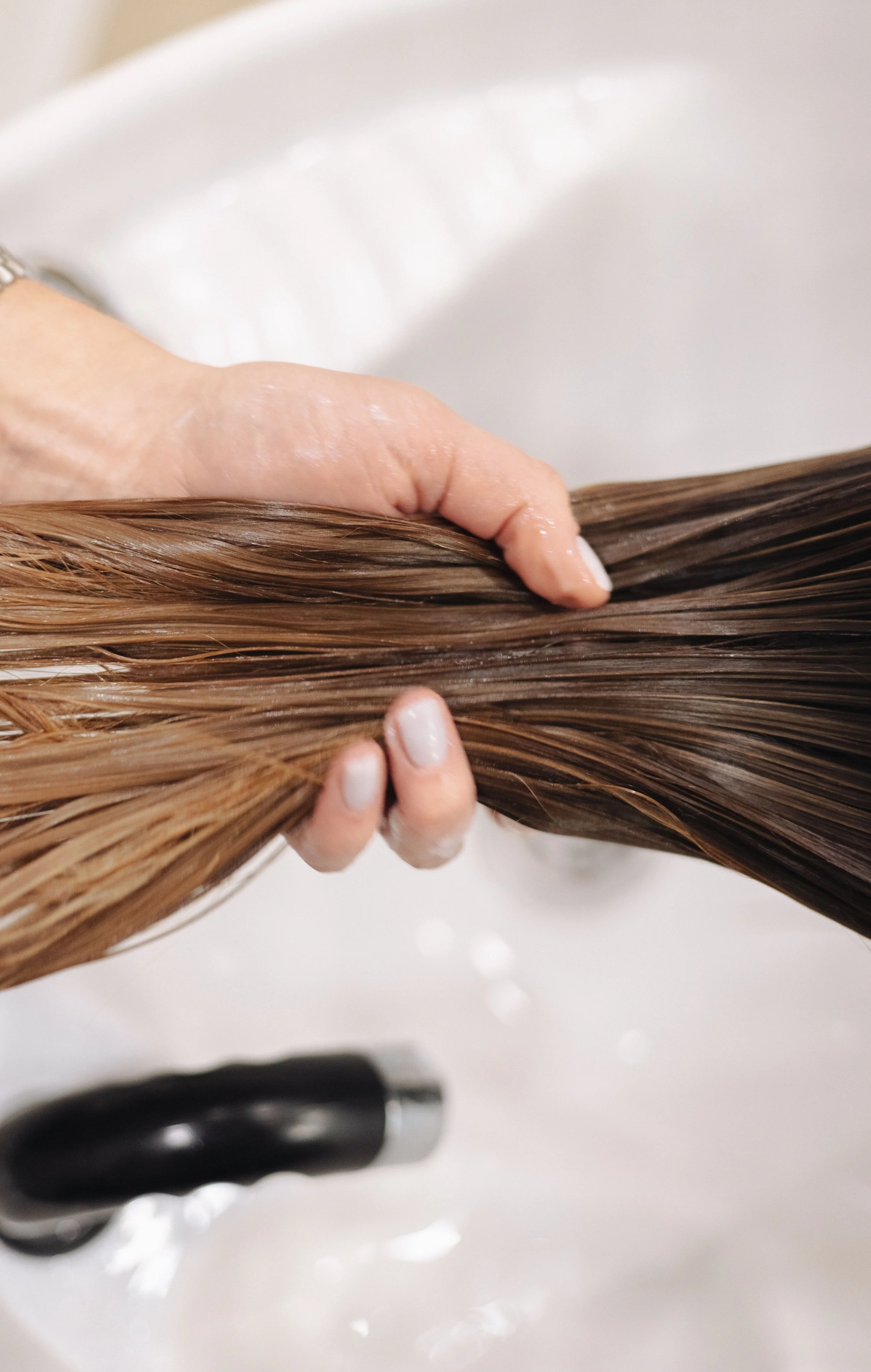 Person washing long, light brown hair in a sink with water, using their hand to massage and rinse the hair.