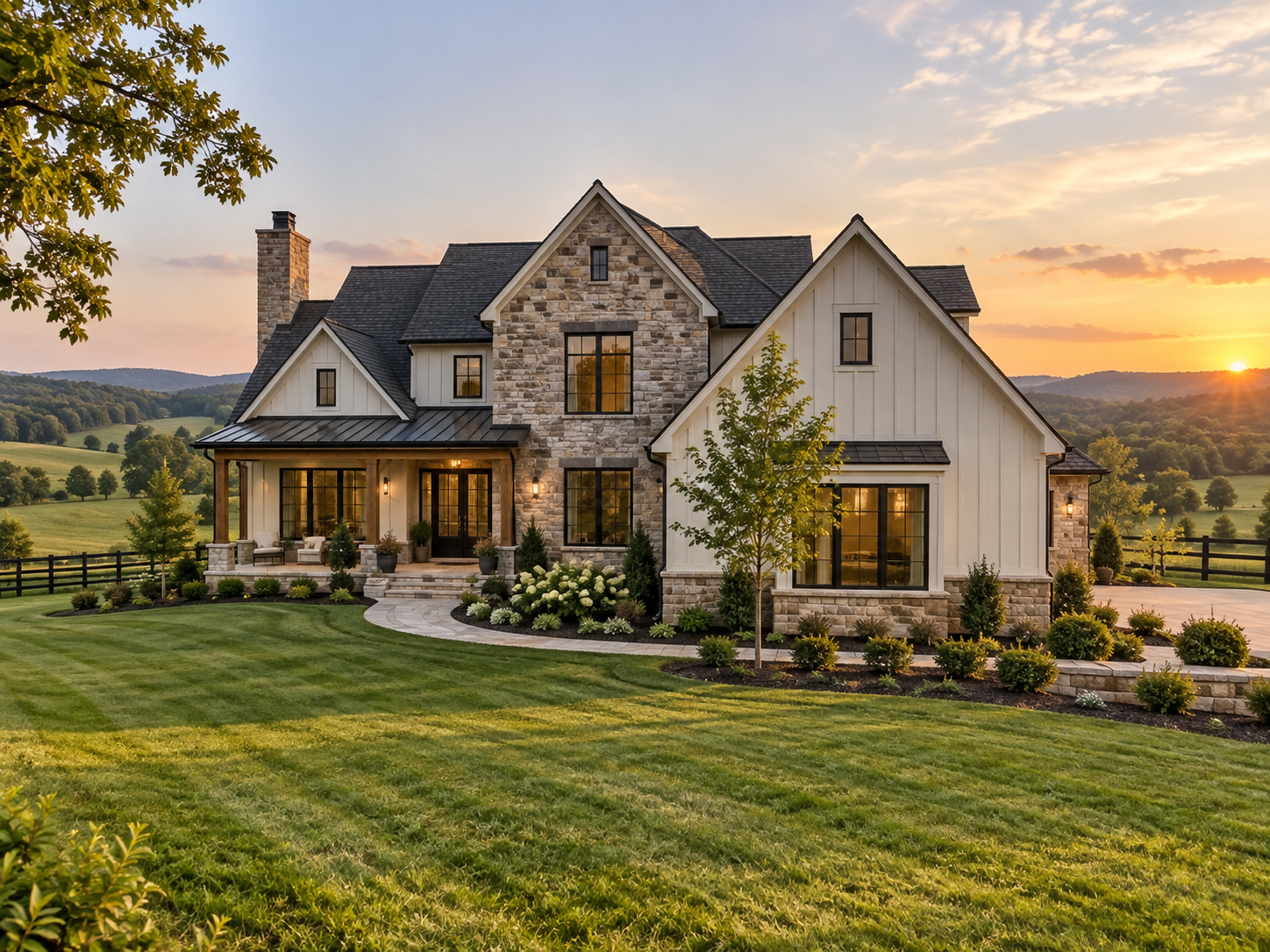 A large, modern house with a stone and white siding exterior, surrounded by a well-maintained lawn and landscaping, at sunset with rolling hills in the background.