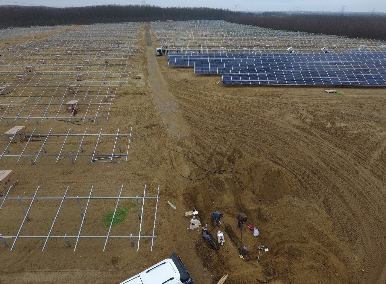 Construction of a solar panel farm with some panels installed and some frames waiting to be installed, along with workers working on the site.