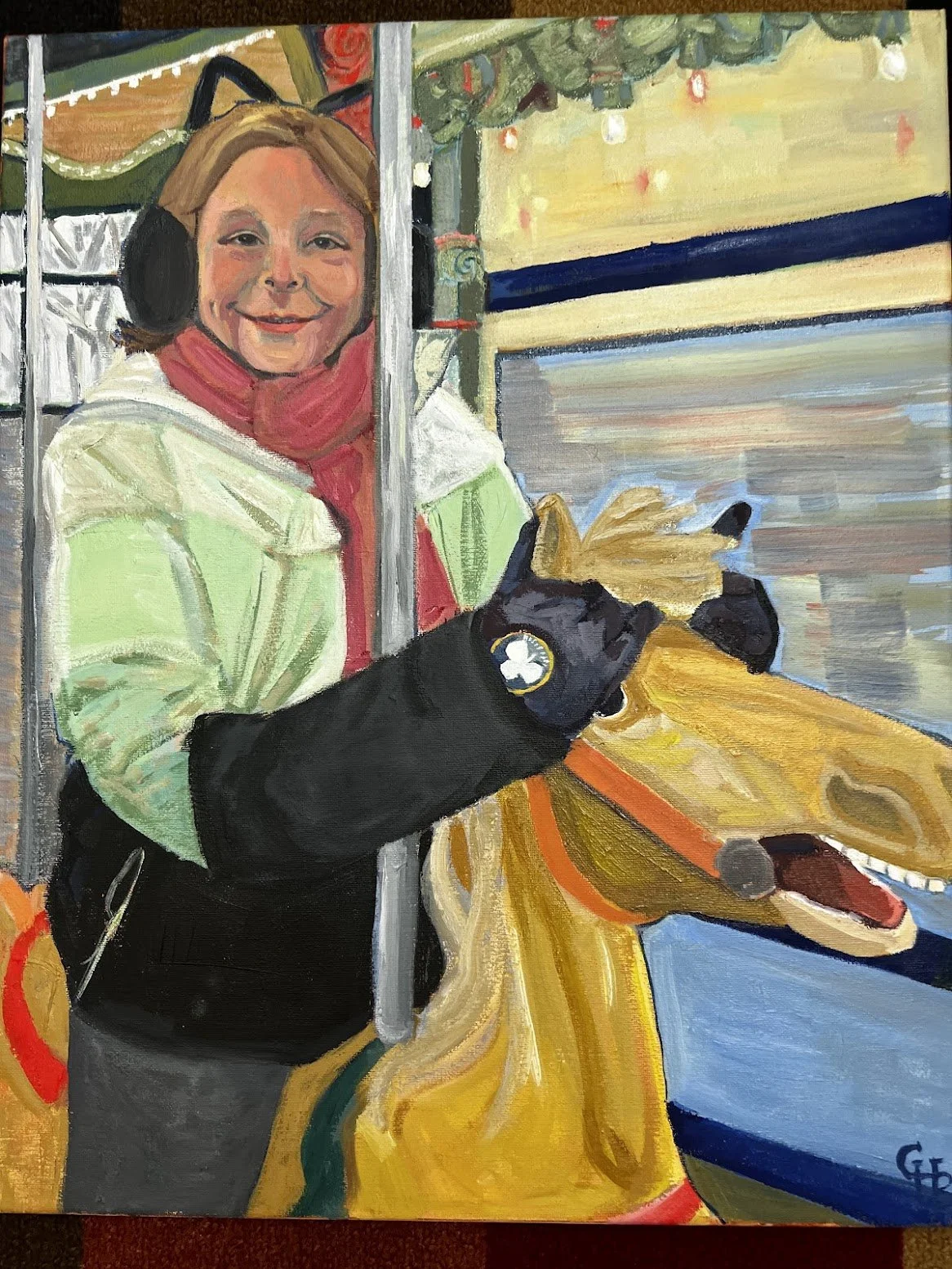 A young girl wearing a black cat ear hat, pink scarf, and winter jacket rides a carousel. The scene is decorated with string lights and festive decorations.
