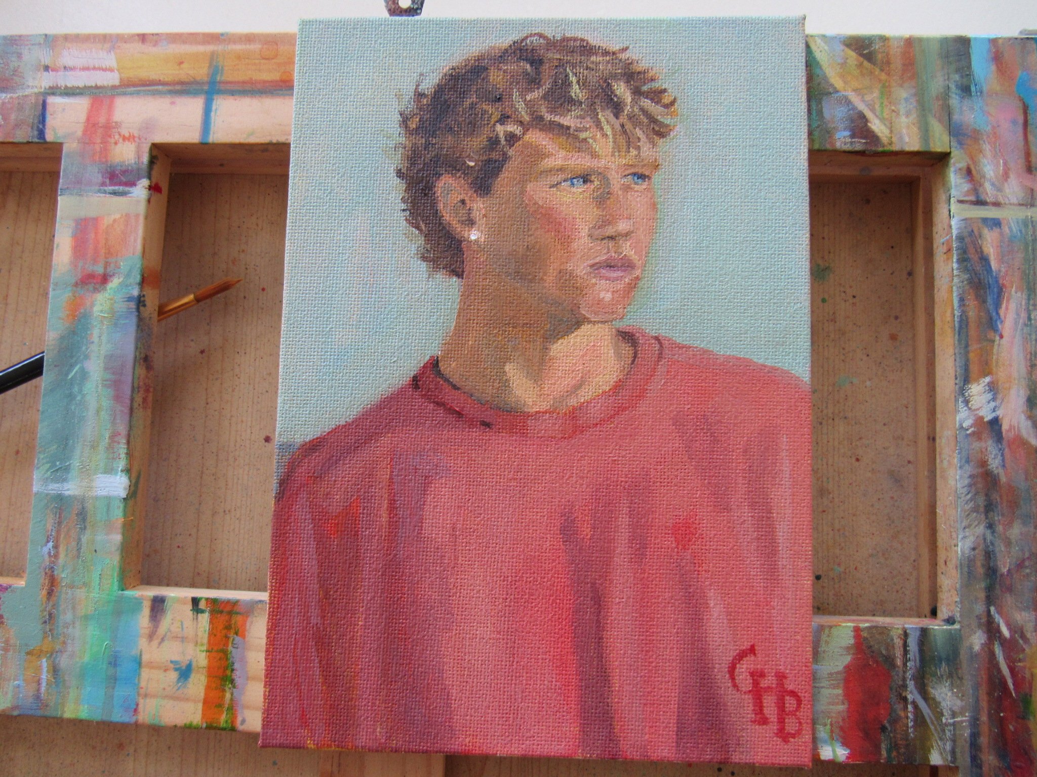 Close-up of a portrait of a teen boy with short, curly hair wearing a red shirt, oil-painted on canvas board.