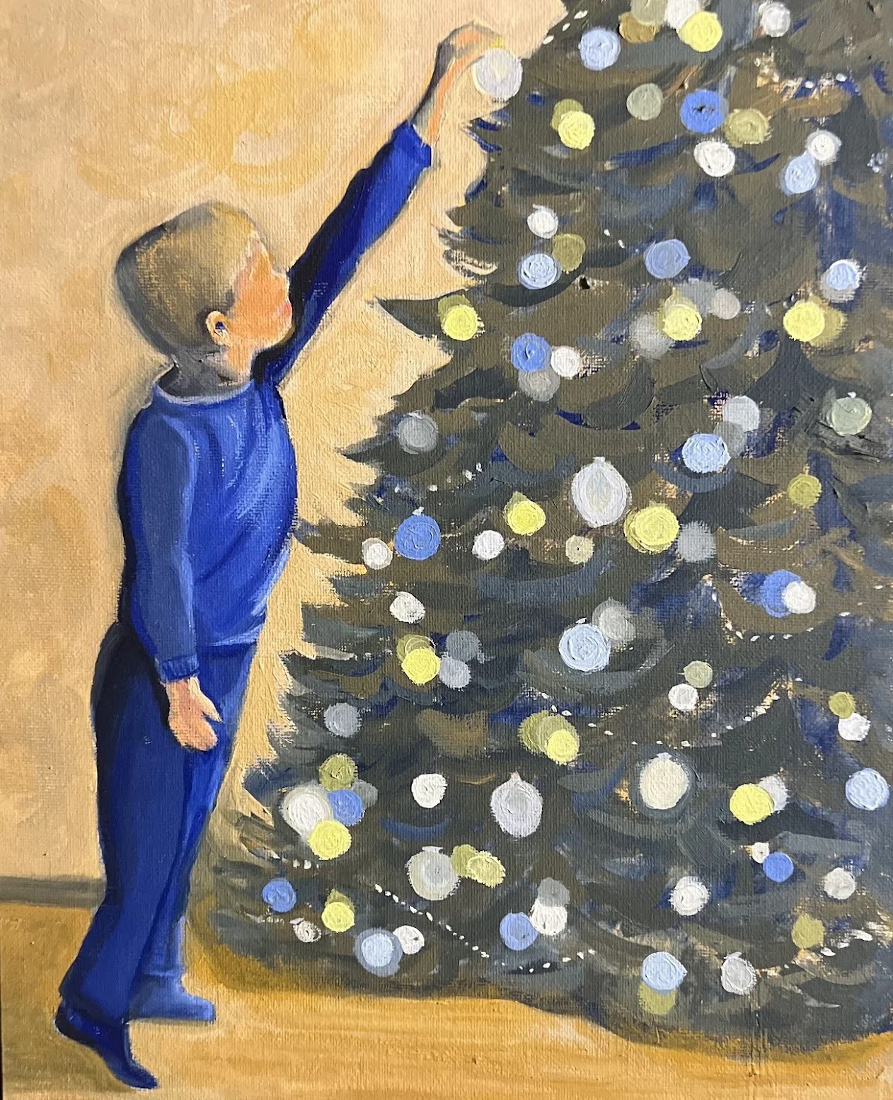 A boy dressed in blue is reaching up to decorate a Christmas tree with lights and ornaments in an indoor setting.