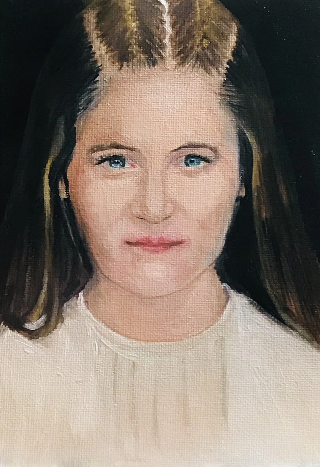Close-up of a teen girl's face with blue eyes, medium-length brown hair, and light makeup, wearing a cream-colored top.