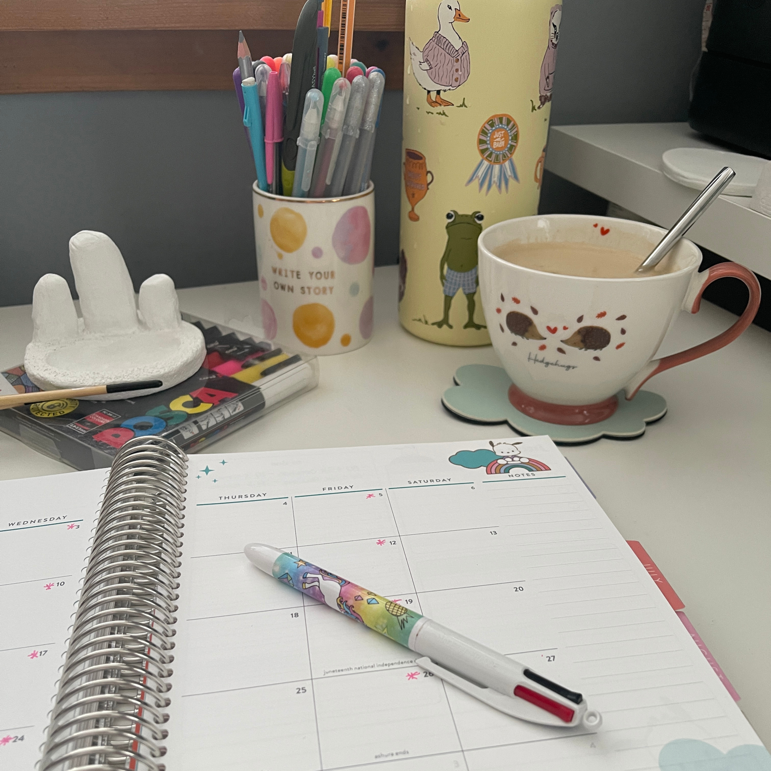 Desk with pens in a cup, a calendar, a bowl of coffee, and stationery items.