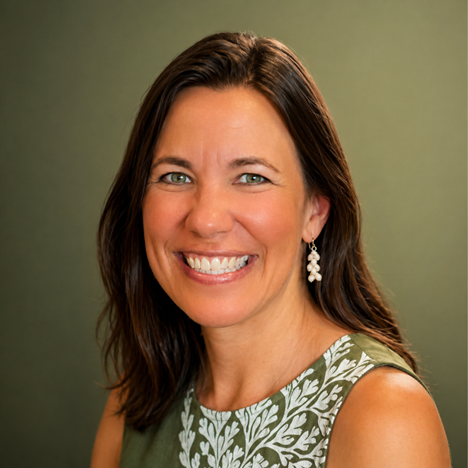 Portrait of a smiling woman with brown hair wearing a sleeveless green top with white embroidery and dangling earrings, against a green background.