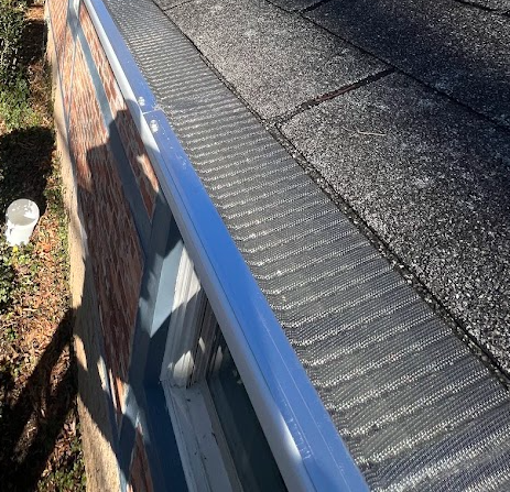A close-up of a house's roof edge with shingles and a blue gutter.