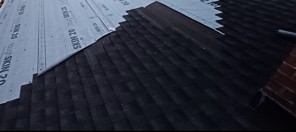 Black asphalt shingles on a roof with some underlayment visible at the top edge.