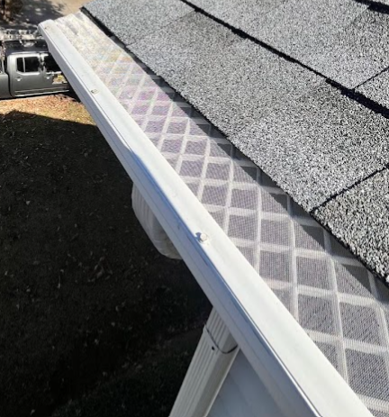 Close-up of a house roof with newly installed asphalt shingles and a metal gutter.