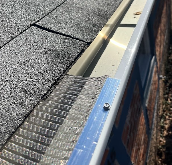 Close-up of a roof edge showing asphalt shingles, metal drip edge, and part of a building wall.