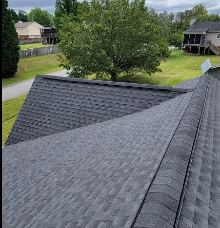 View of a roof with asphalt shingles, with a tree and neighboring houses in the background.