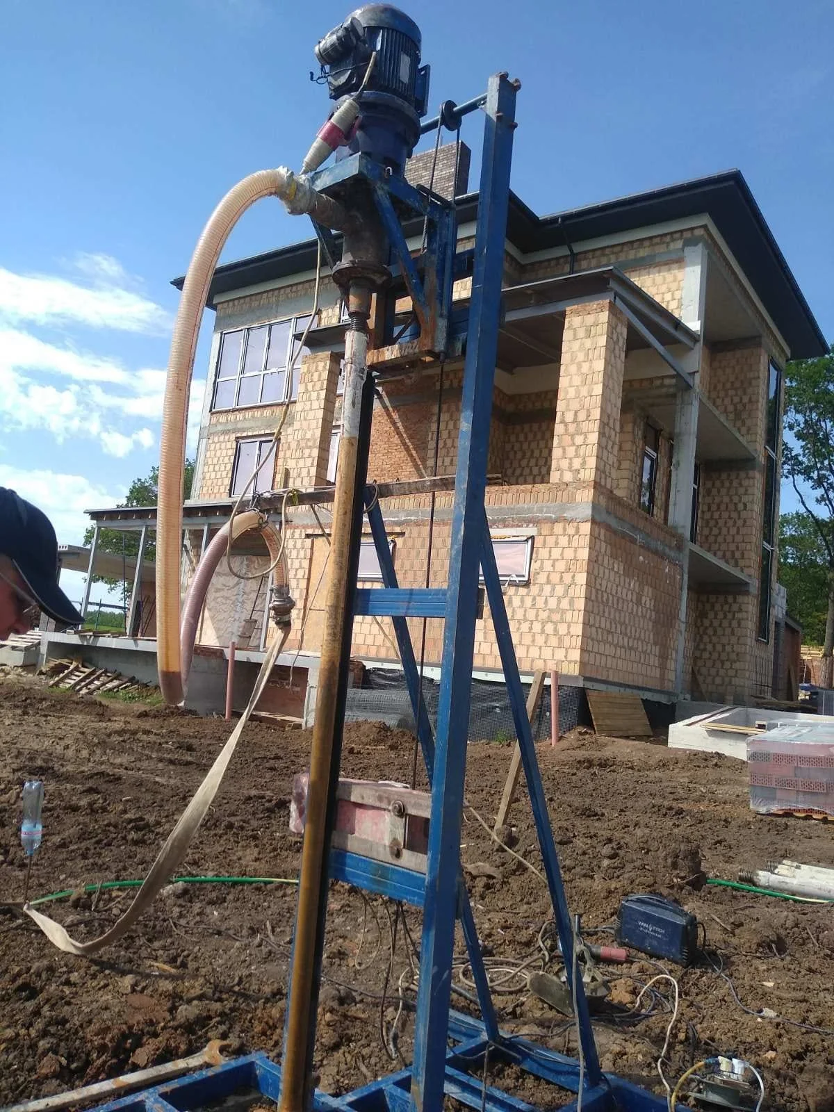 Construction site with a brick house being built, construction equipment, and scaffolding in front. The sky is blue with some clouds.